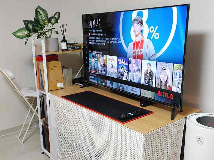 ナチュラルウッド調のリビング、50インチスマートテレビとパソコンデスクが配置された清潔感のある空間