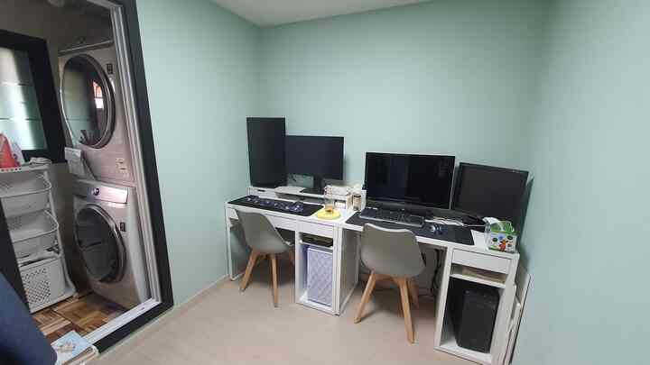 Compact home office workspace with white furnishings and wood tone flooring, featuring four well-arranged monitors for productivity