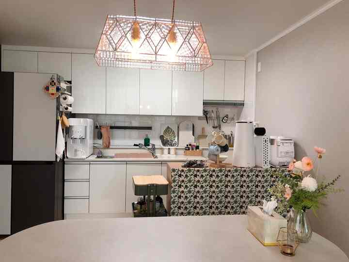 White-toned kitchen and dining room featuring pendant lights, dining table, and a vase with flowers in a cozy modern space