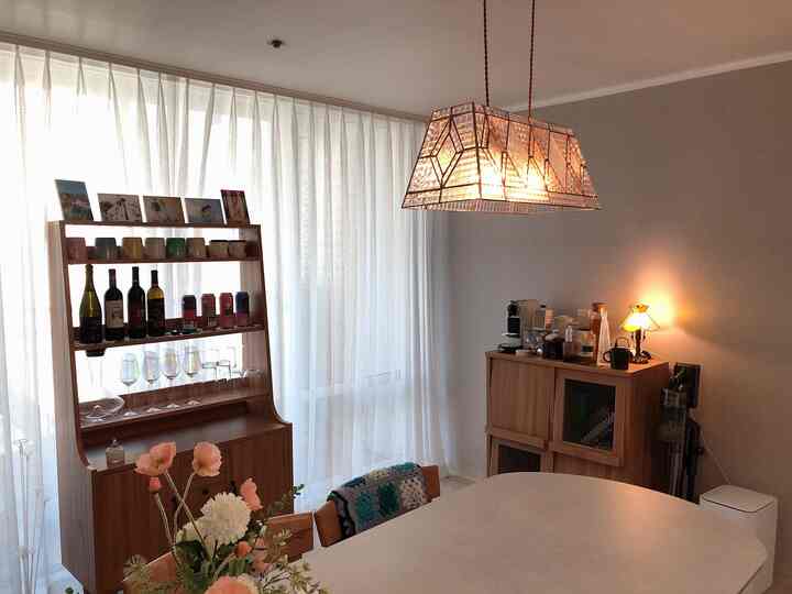 Natural-toned dining room with white curtains, wood furniture, dining table, and warm pendant lighting creating cozy atmosphere