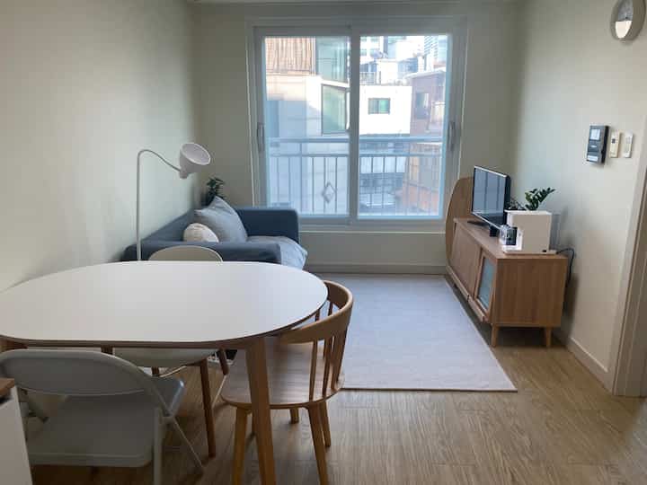 ホワイトとウッドトーンが調和したミニマルな二人暮らし向けリビング、楕円形テーブルとソファが配置された印象的な空間