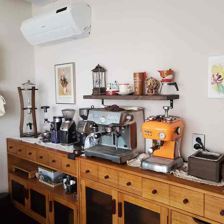 White background wall and wooden console buffet topped with various coffee machines and framed art, featuring Ascaso and Breville machines in a cafe-style home cafe space