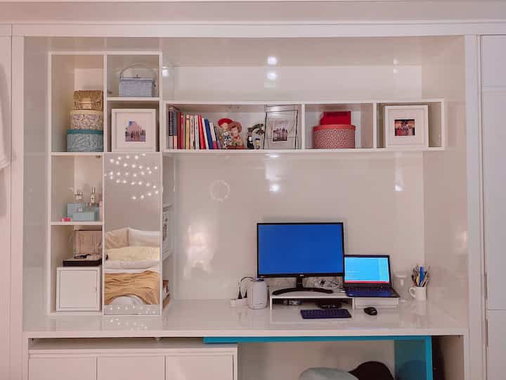 White-toned home office space featuring open shelves, monitor setup and desk, creating a clean and bright atmosphere