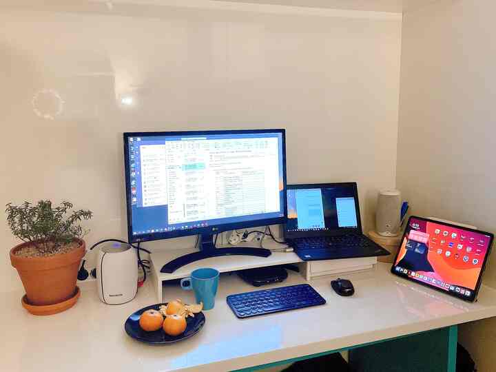 ホワイトトーンのホームオフィス、モニタースタンドと植物、みかんの置かれた清潔なデスク