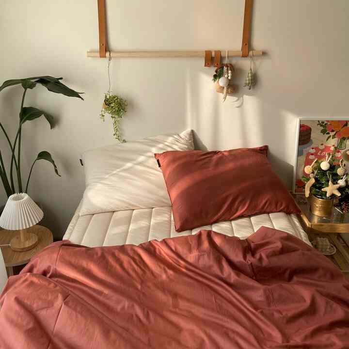 暖かいナチュラルトーンの寝室で、ベージュと赤の寝具が配置された落ち着いた空間