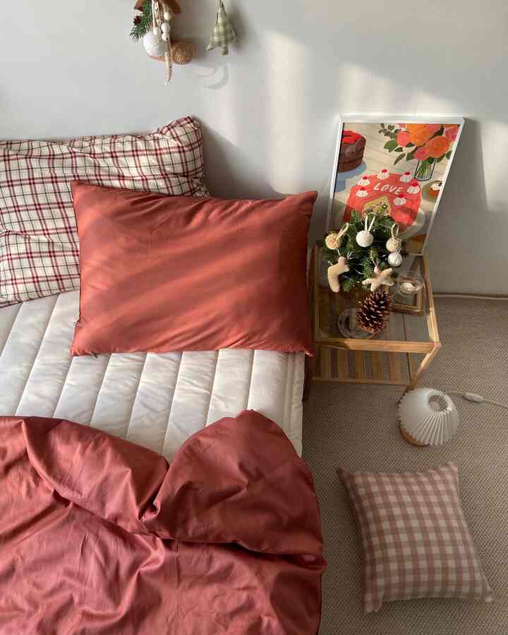 Warm orange and beige toned bedroom featuring checkered pillows and a wooden side table in a cozy arrangement