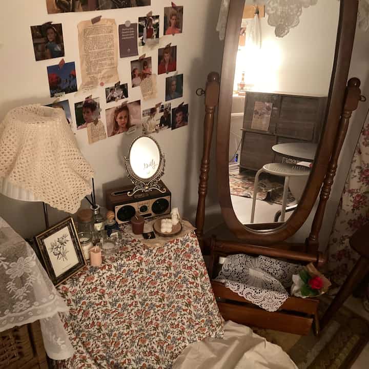 Brown-toned vintage style space featuring a full-length mirror, lace-covered table, and assorted decor items creating a cluttered atmosphere