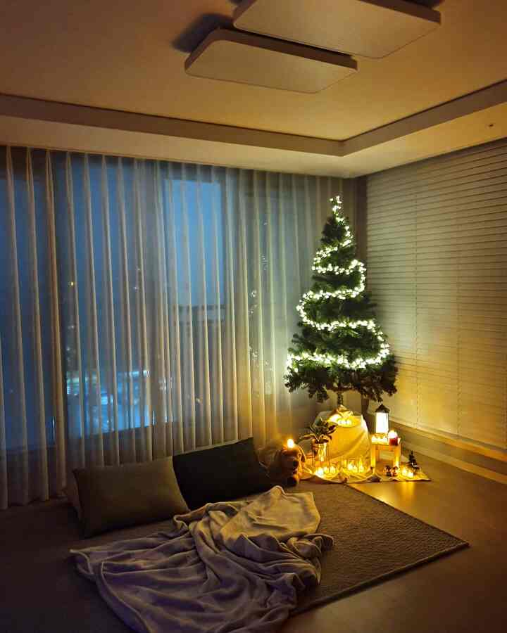 Cozy white-toned living room featuring a decorated Christmas tree, warm lighting, dog plush, and pillows