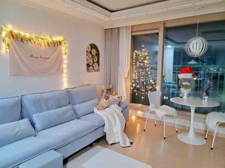 白と青のトーンのリビング、広い青のソファと円形テーブル、ストリングライトのクリスマスツリーが温かいクリスマスの雰囲気を醸し出すインテリア