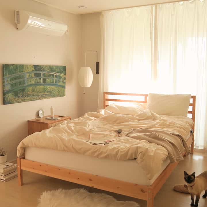 アイボリーと木目調の調和が取れた寝室、ベージュの寝具とモネの額入り絵画が温かみのある雰囲気を演出