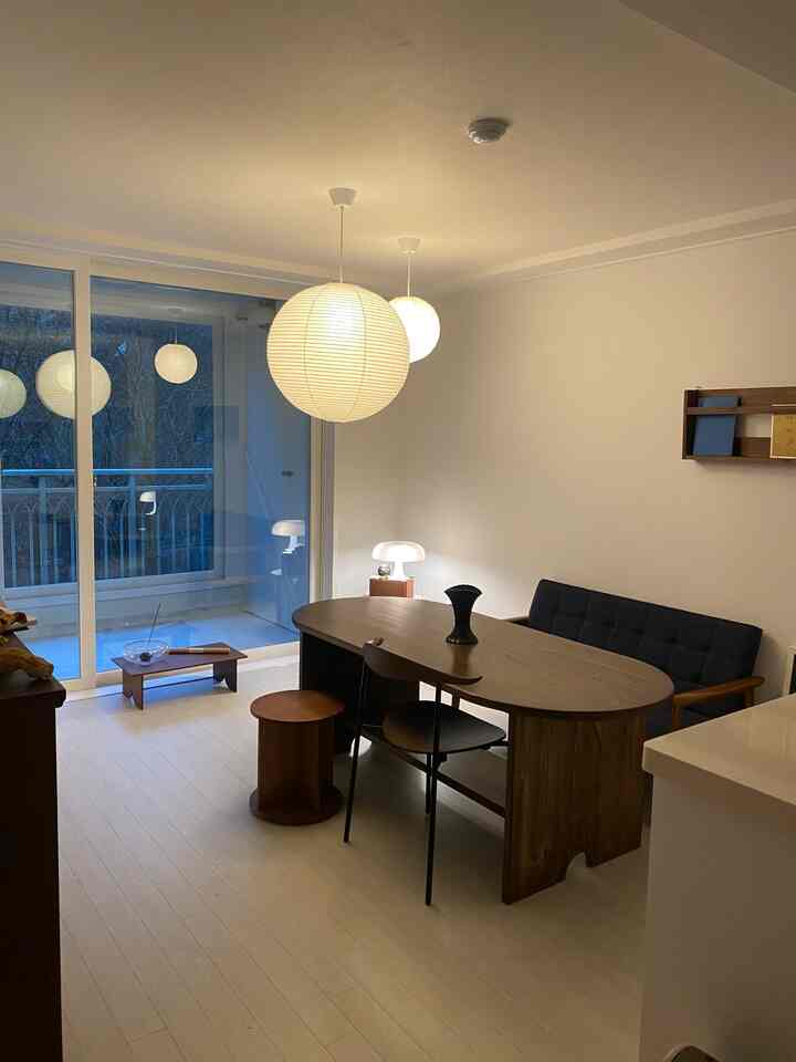 明るい白色のダイニングルーム、木製のダイニングテーブルと黒い椅子、2つの丸いペンダントライトが配置されたナチュラルモダンな空間