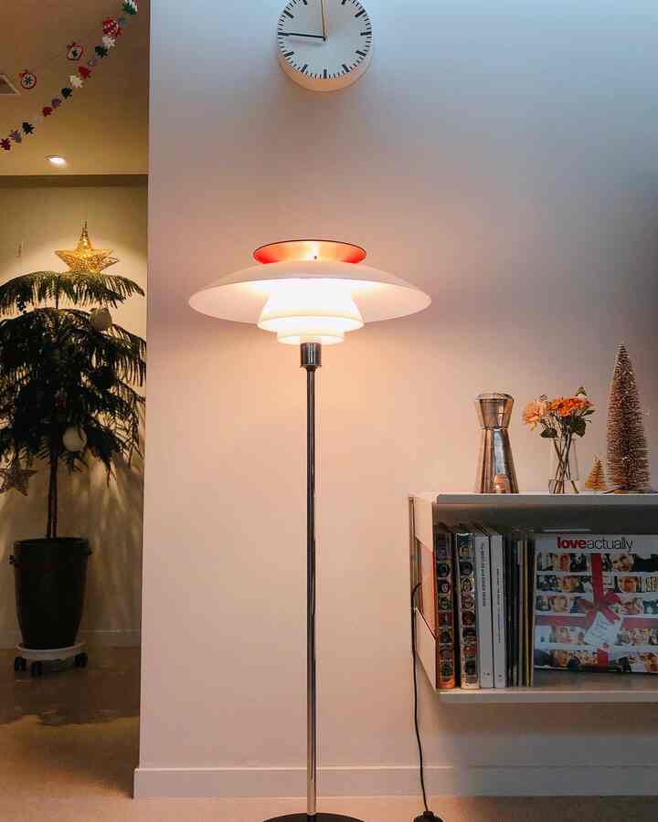 白を基調としたリビングルームにフロアランプと壁時計、本棚が配置され、間接照明で落ち着いた雰囲気のインテリア