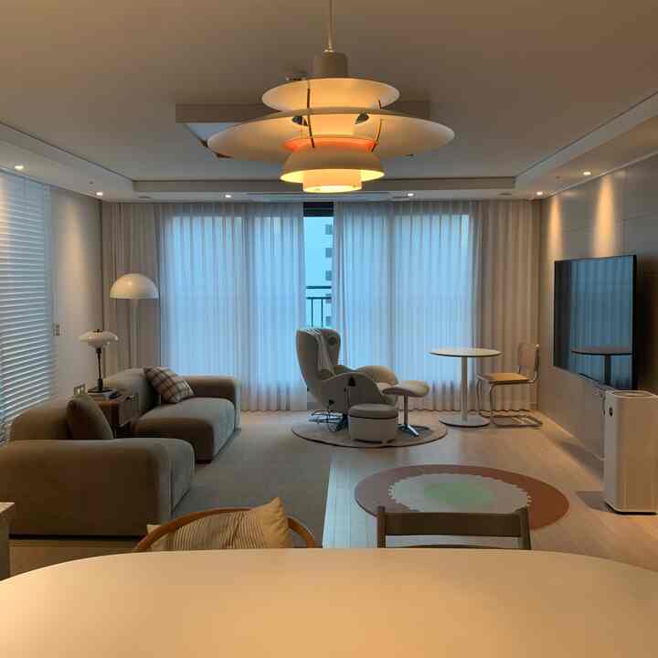 A white and brown natural tone living room featuring a large sofa, massage chair, round rugs, and pendant lighting creating a warm and cozy atmosphere