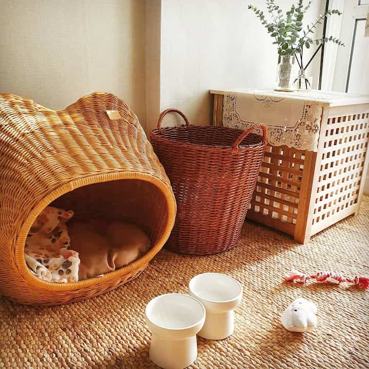 Natural-toned corner featuring rattan pet house, laundry basket, and pet toys on woven floor, creating a cozy pet space
