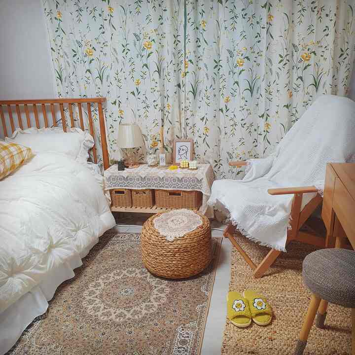 Beige-toned bedroom featuring natural wood furniture, floral curtains, cozy armchair, and rug, creating a warm and inviting interior