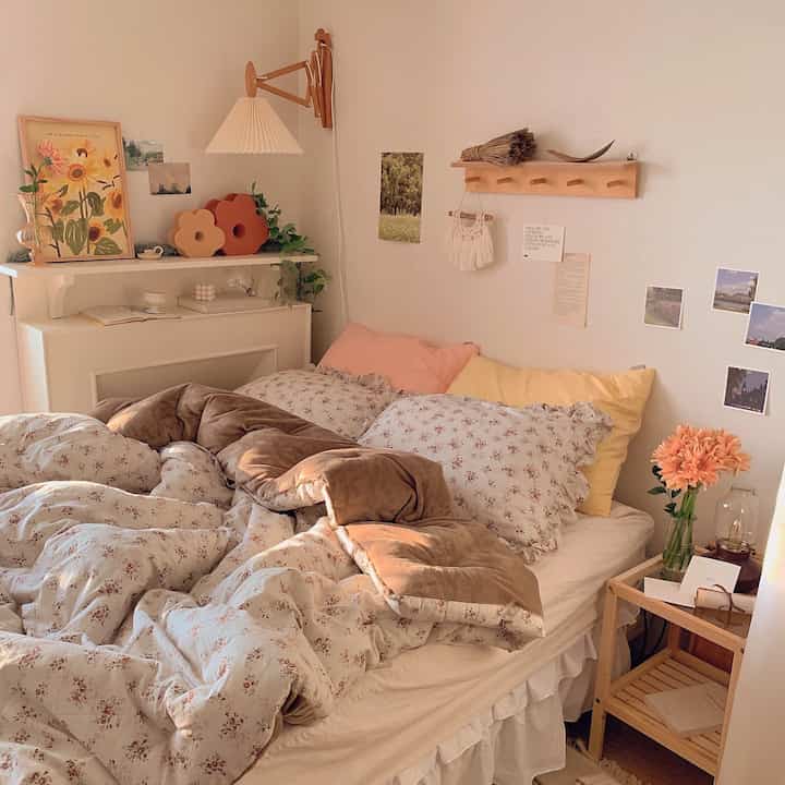 Warm beige and brown toned bedroom featuring floor lamp, wooden nightstand, vase with flowers, and wall decor creating cozy atmosphere