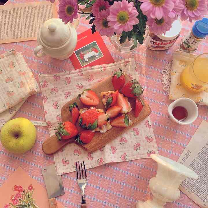 Strawberry pink toned home cafe table featuring wooden tray with strawberry croffle, teapot, and vase creating cozy vibes