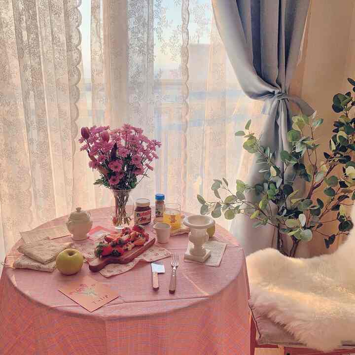 Natural home cafe space featuring a pink-tone round table, lace curtains illuminated by warm sunlight