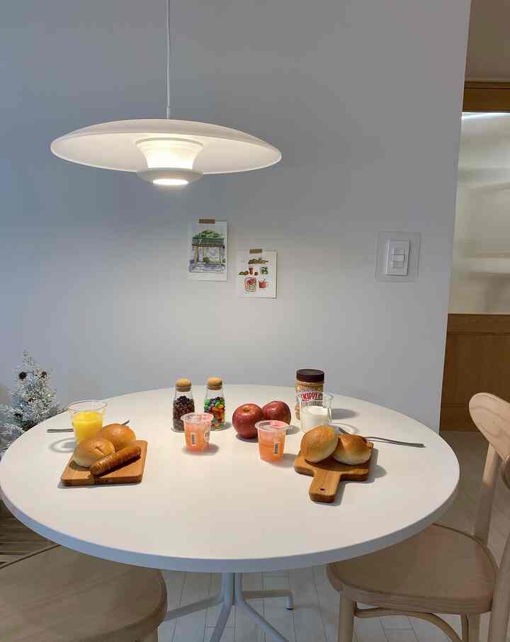 A simple and cozy dining room in white and natural tones featuring a round dining table with natural wood chairs