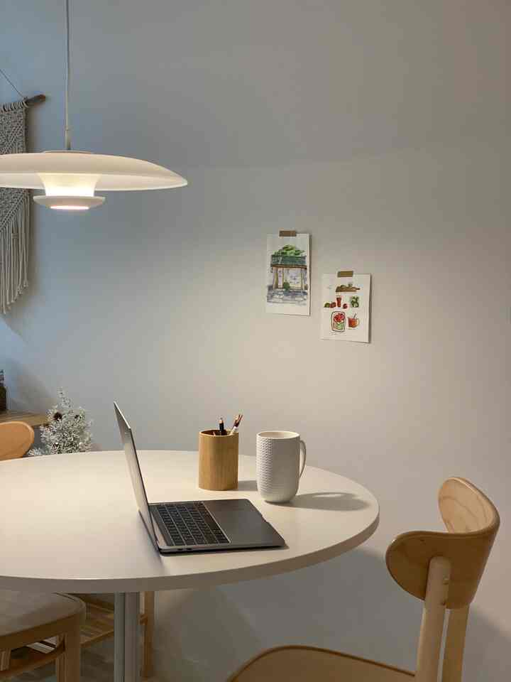 White and wood tone round dining table space featuring a laptop and cup, creating a simple and functional kitchen interior
