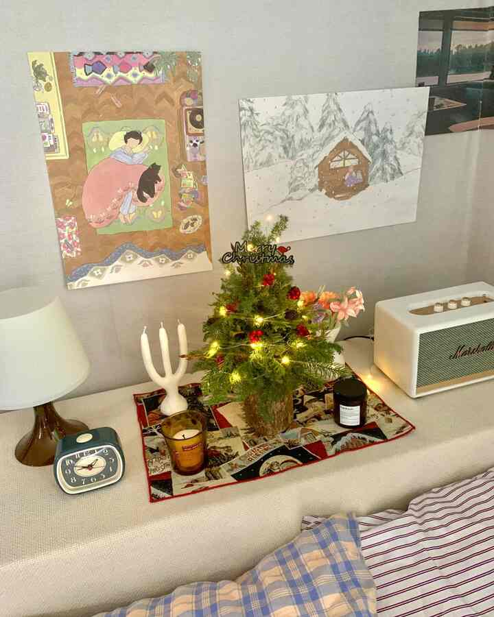 Beige-toned bedroom space featuring blue patterned bedding and a decorated mini Christmas tree in a cozy studio apartment interior
