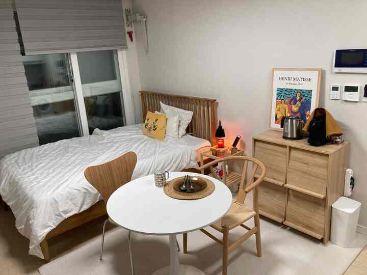 A white and wood tone studio apartment featuring a bed, dining table, and coffee machine with a cozy atmosphere