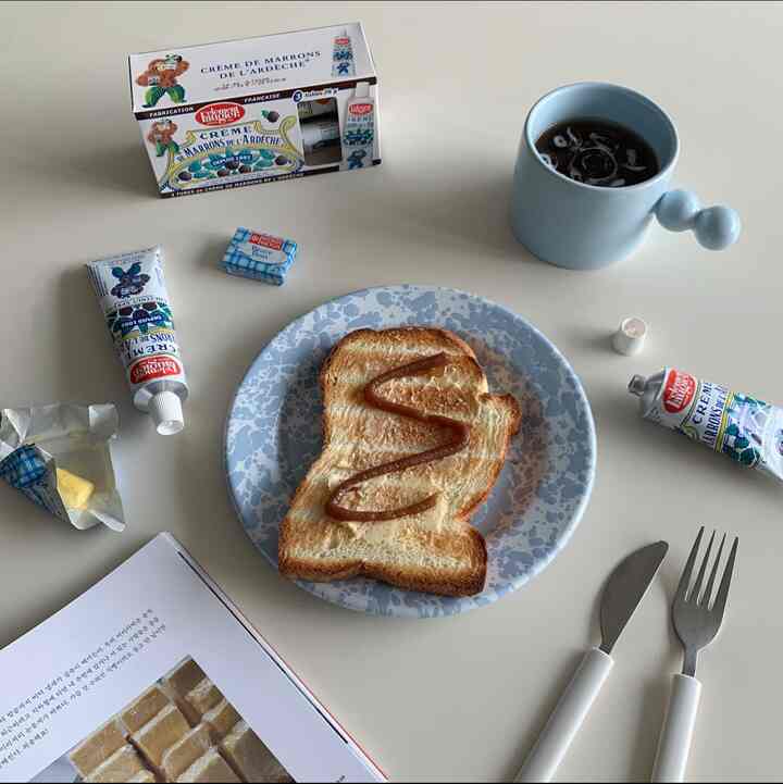 ベージュのテーブルに青いマーブル柄の皿とトースト、ジャムチューブ、青いマグカップが置かれた雰囲気のあるキッチンインテリア