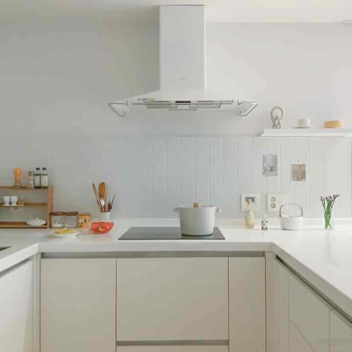 White and natural wood-tone kitchen without upper cabinets, with a clean countertop featuring a pot and kitchen utensils centrally placed