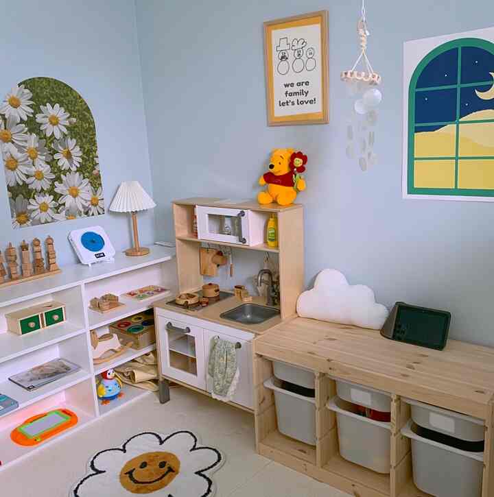White and natural wood toned kids' room featuring toy kitchen, storage bins, posters creating a cozy playful atmosphere