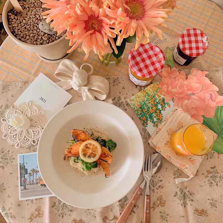 Orange and salmon-toned home cafe dining table featuring salmon cream risotto, flowers, and jam jars in a cozy setting