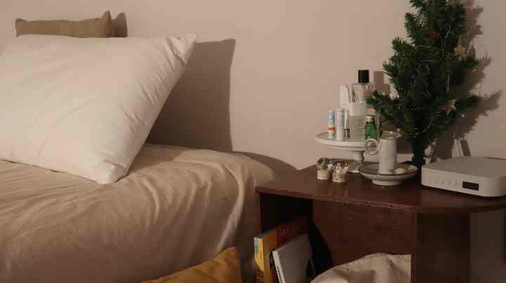 Cozy beige-toned bedroom featuring a bed with pillow and blanket, and a small Christmas tree on a wooden side table creating a natural atmosphere