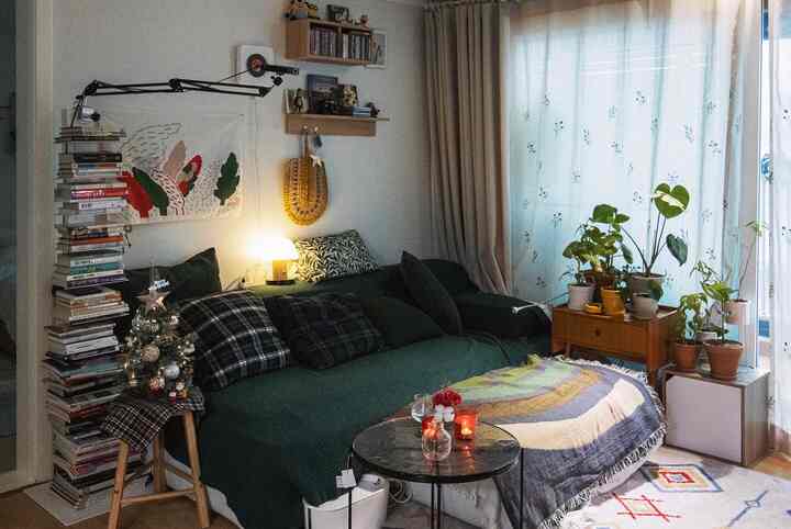 Deep green toned living room featuring a central sofa, warm lighting, Christmas tree, and plants creating a cozy atmosphere