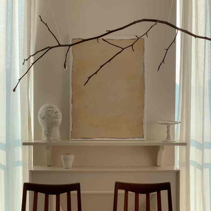 Living room in white and beige tones featuring a fireplace shelf with artwork and sculptural objet, showcasing a natural interior