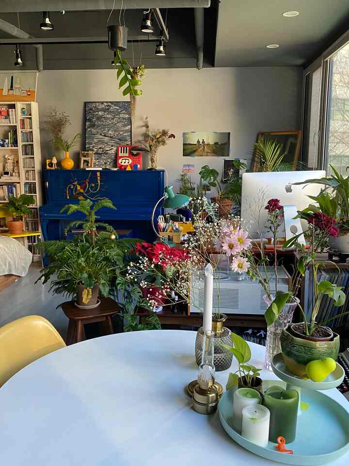 White round table with abundant plants in living room featuring blue piano and bookshelf, creating natural modern space