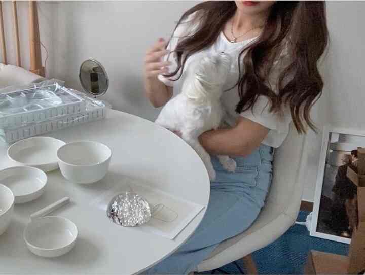 Simple and cozy living room in white and blue tones, featuring a round dining table and a woman holding a dog