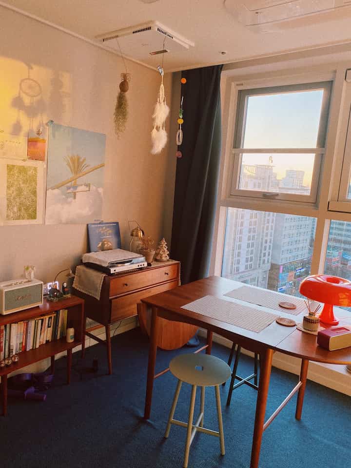 暖かいオレンジ色の照明とブルーのラグが映えるダイニングルーム、窓の外には夕日の風景が広がる雰囲気のあるインテリア