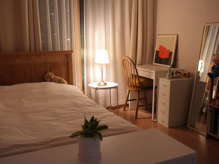 Warm toned bedroom featuring a wooden bed, desk, curtains, and soft lighting creating a cozy student space