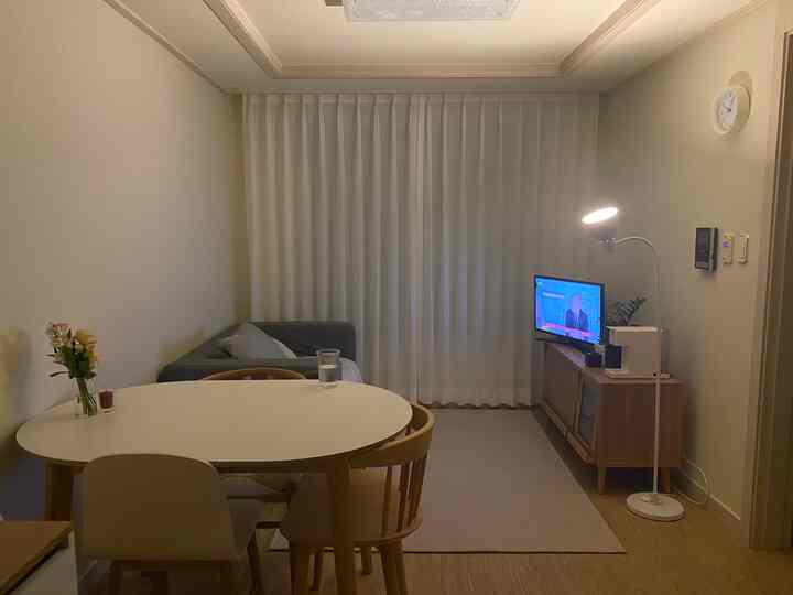 Modern studio apartment living room with white and wood tones, featuring curtains and dining table in a cozy setting