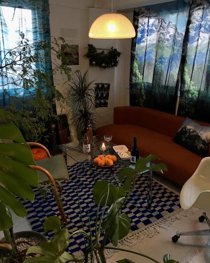 青い山と森のカーテン、茶色のソファと植物が配置された雰囲気のあるリビング