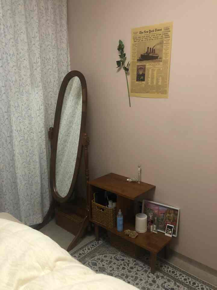 暖かいナチュラルトーンの寝室、木製の全身鏡とサイドテーブルが配された雰囲気のあるインテリア