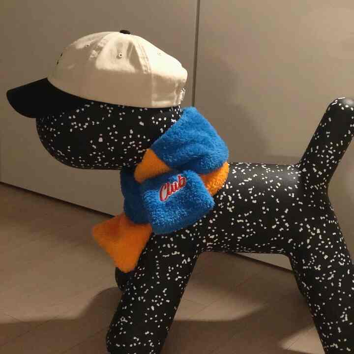 Black dog-shaped objet with white spots, adorned with blue and orange scarf and white cap, cute toy figure indoors