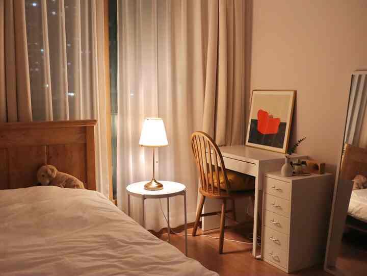 Cozy bedroom for one featuring warm wood tones and white furniture, with curtains and soft lighting enhancing the atmosphere