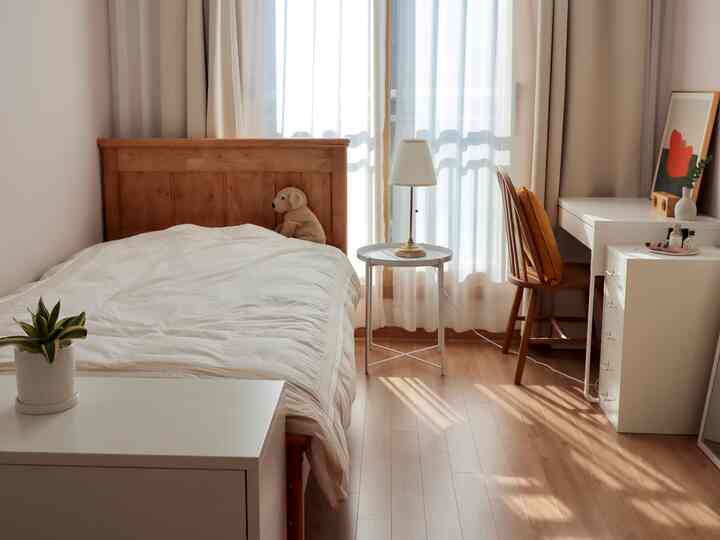 A white and wood-tone bedroom featuring a bed, desk, and dresser creating a warm and cozy atmosphere
