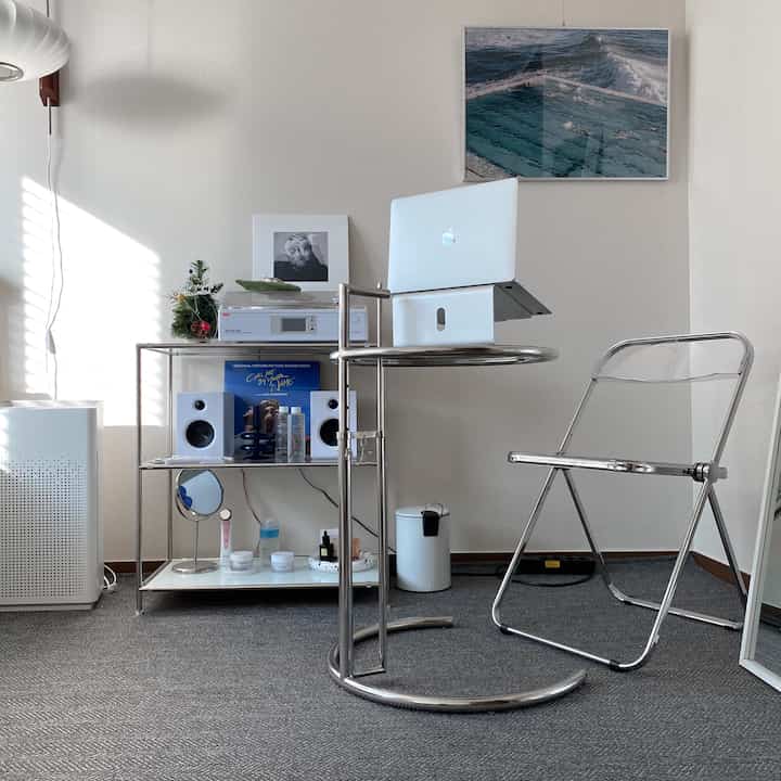 Minimal home office with white walls and gray rug, featuring chrome desk and transparent chair