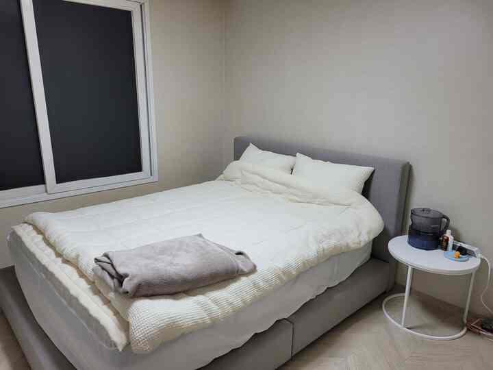 白とグレーのトーンの寝室、大きなベッドとナイトテーブルが配置された落ち着いたシンプルな空間