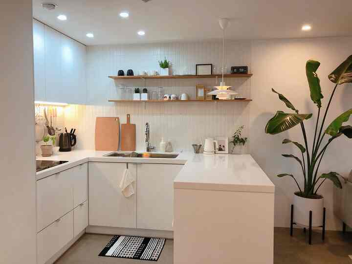 Minimal kitchen without upper cabinets in white and wood tones, featuring a clean island and home cafe accessories on shelves