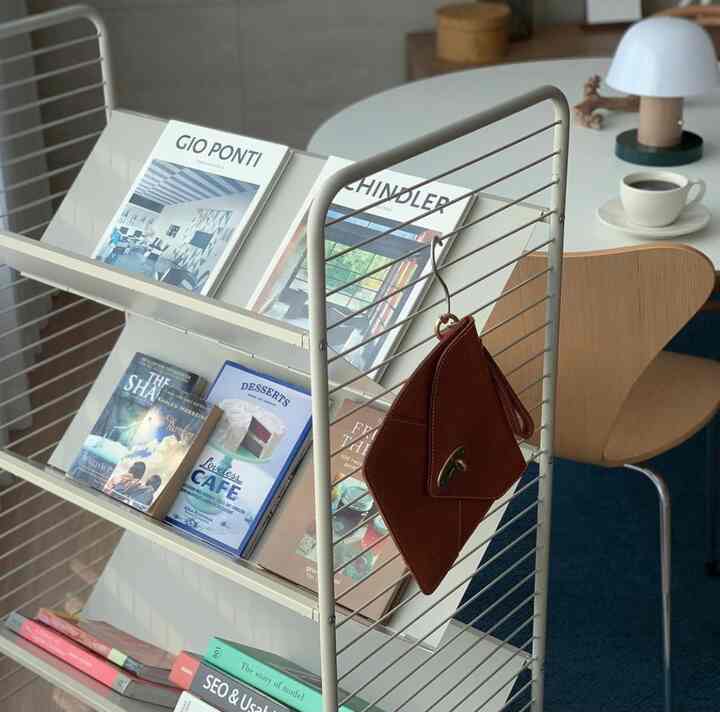 Cafe-style study space with a blue rug and wooden chair, featuring a trolley bookshelf and coffee cup accessories in a cozy interior