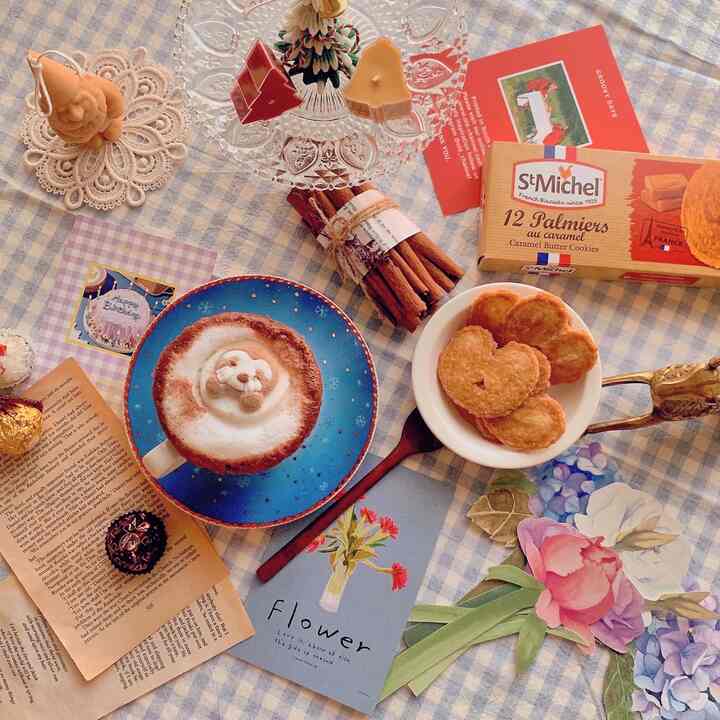 Beige and brown toned home cafe setting featuring a hot chocolate with bear-shaped foam, cookies, and Christmas-themed decorative items creating a cozy atmosphere