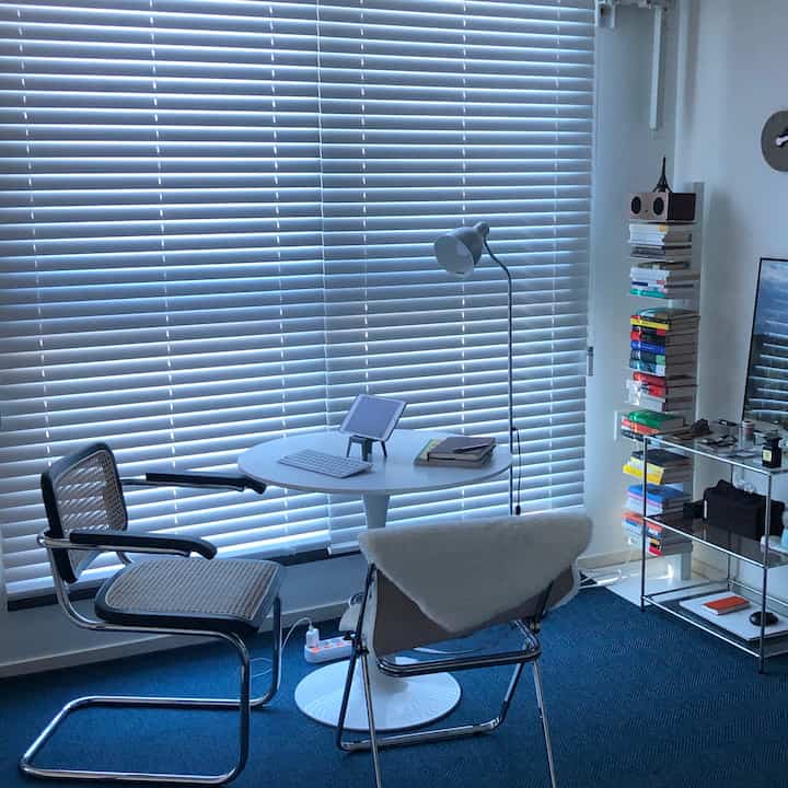 A neat home office with navy rug and wood-tone chairs, large wooden blinds dominating the space atmosphere