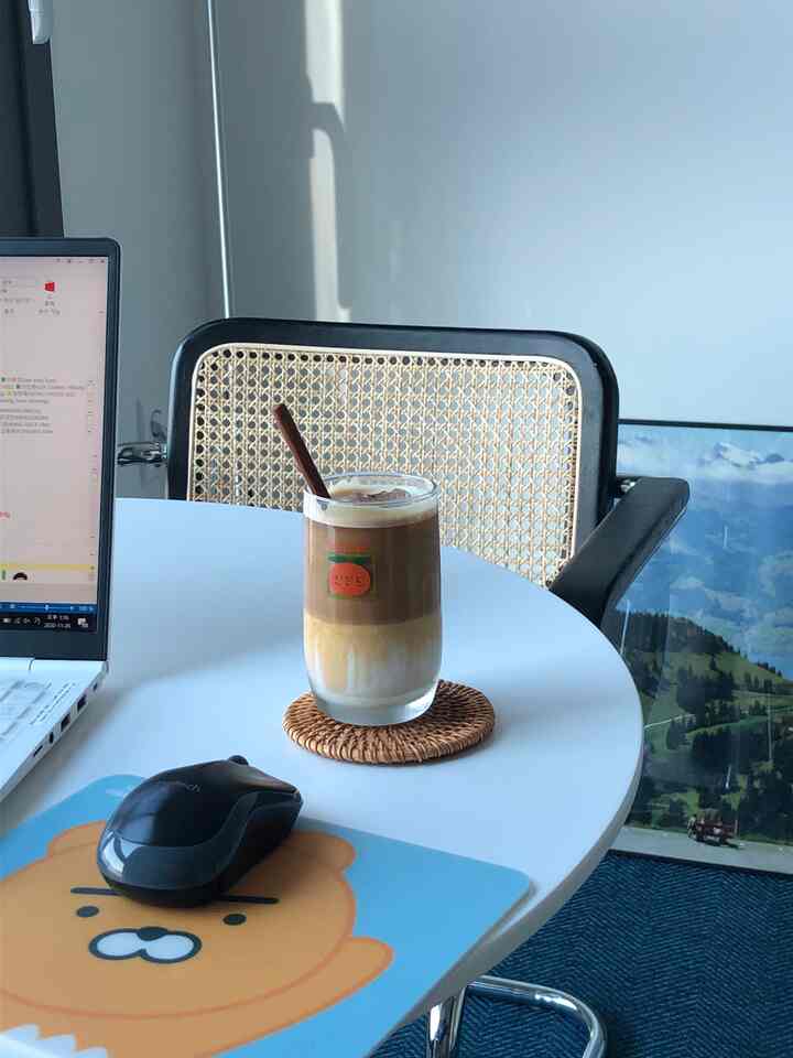 A home office space with white walls and table, featuring a rattan armchair and iced coffee on a round desk creating a cozy atmosphere